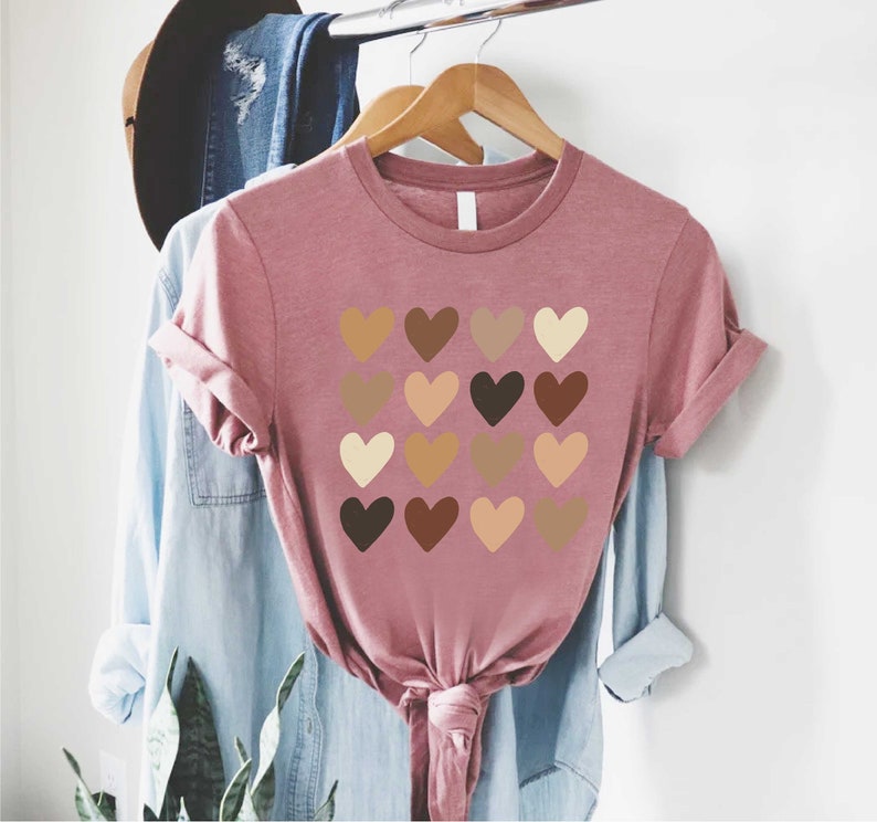 May include: A pink t-shirt with a design of 16 hearts in different shades of brown, representing skin tones.