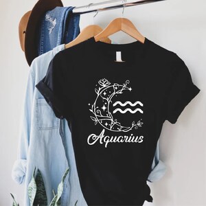 May include: Black t-shirt with a white floral design and the word "Aquarius" printed on the front.