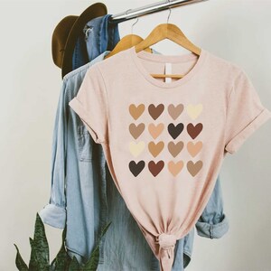 May include: A pink t-shirt with a graphic of a square of hearts in various shades of brown. The hearts are arranged in a grid pattern.