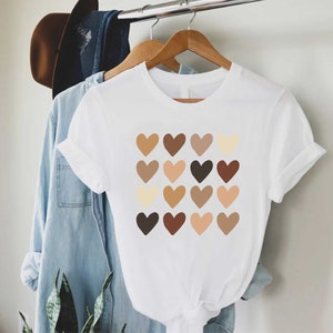 May include: White t-shirt with a graphic of a grid of 16 brown, beige, and cream hearts.