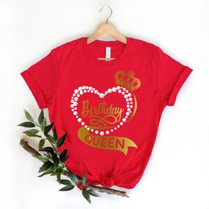 May include: Red t-shirt with a gold heart design that says "Birthday Queen" with a crown on top. The heart is surrounded by white pearls.