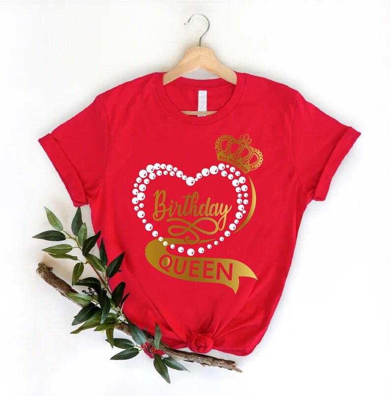 May include: Red t-shirt with a gold heart design that says "Birthday Queen" with a crown on top. The heart is surrounded by white pearls.