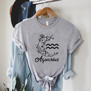 May include: Gray t-shirt with a black graphic of a crescent moon with stars and vines, and the word "Aquarius" underneath.