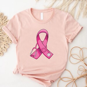 May include: Pink ribbon with a stethoscope on a light pink t-shirt.