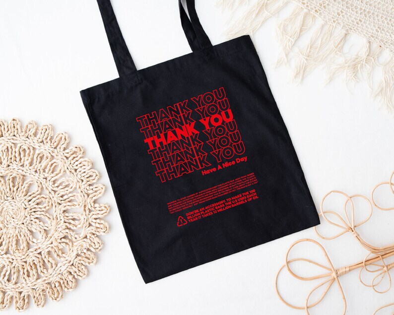 May include: Black tote bag with red text that says "Thank You" repeated multiple times. The bag also has the text "Have A Nice Day" printed on it.