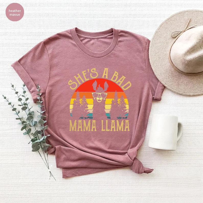 May include: A heather mauve t-shirt with a retro sunset graphic featuring a llama wearing sunglasses and the text "She's a Bad Mama Llama".