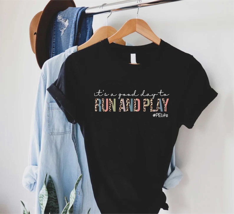 K&ouml;nnte beinhalten: Schwarzes T-Shirt mit dem Text "it's a good day to RUN AND PLAY" in bunten Buchstaben mit Leopardenmuster. Der Text "#PELife" befindet sich unter dem Haupttext.