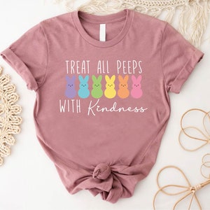 May include: A pink t-shirt with a white graphic of rainbow-coloured peeps and the text "Treat all peeps with kindness".