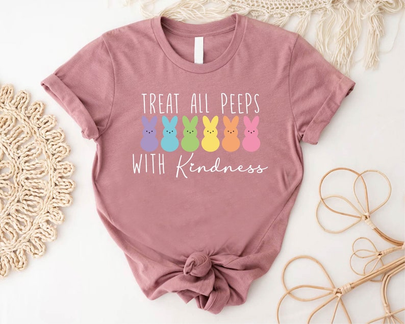 May include: A pink t-shirt with a white graphic of rainbow-coloured peeps and the text "Treat all peeps with kindness".