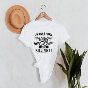 Pode incluir: Camiseta branca com texto preto que diz "Eu n&atilde;o nasci assim, mas aqui estou, 50 anos depois e estou matando".