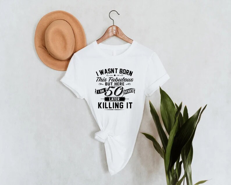 Pode incluir: Camiseta branca com texto preto que diz "Eu n&atilde;o nasci assim, mas aqui estou, 50 anos depois e estou matando".