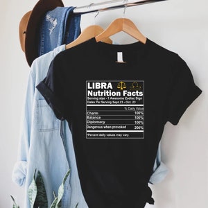 May include: Black t-shirt with a white graphic of a nutrition facts label for Libra, a zodiac sign. The label includes the text "LIBRA Nutrition Facts" and lists the daily value percentages for charm, balance, diplomacy, and dangerous when provoked.