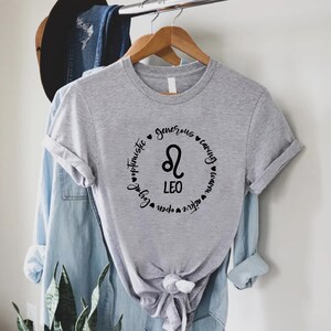 May include: Grey t-shirt with a black circle design featuring the Leo zodiac symbol and the words "Leo", "optimistic", "generous", "caring", "loyal", "open", "active", and "warm".