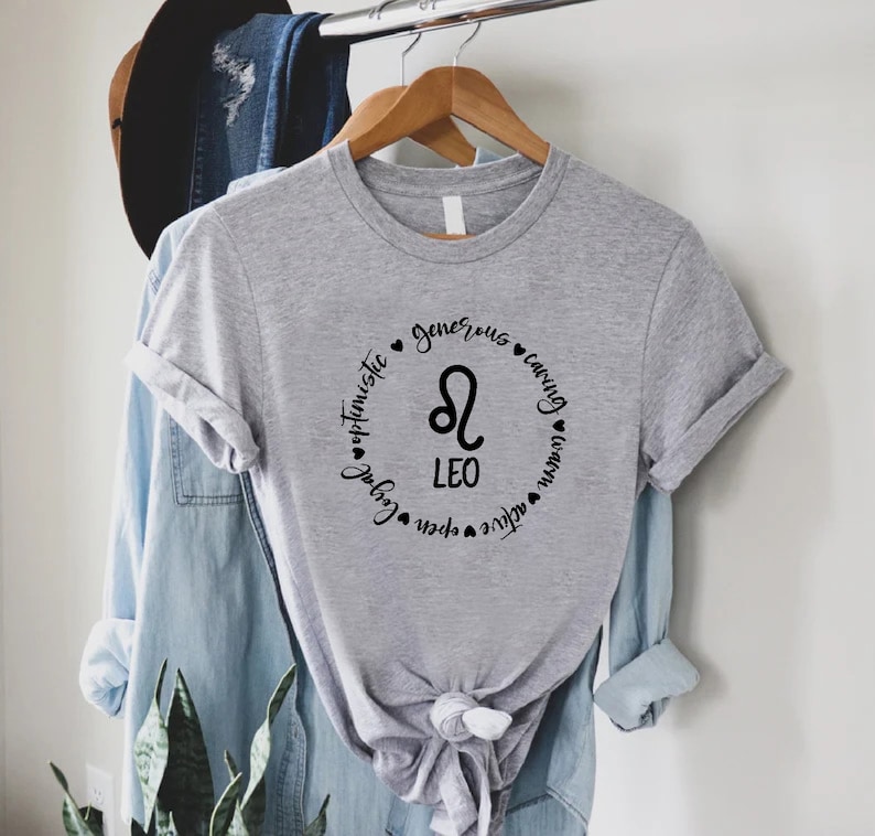 May include: Grey t-shirt with a black circle design featuring the Leo zodiac symbol and the words "Leo", "optimistic", "generous", "caring", "loyal", "open", "active", and "warm".