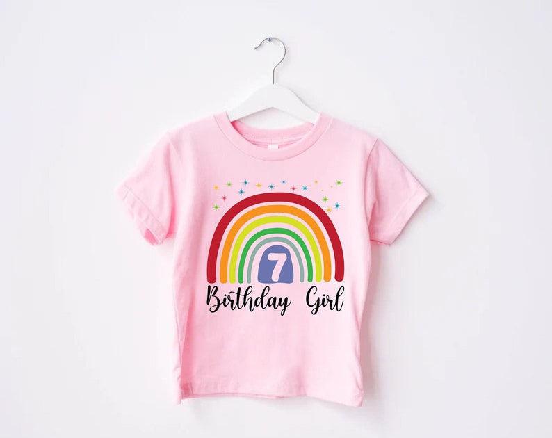 Peut inclure: T-shirt rose avec un arc-en-ciel et le chiffre 7 dans un cercle bleu. Le texte "Birthday Girl" est sous l'arc-en-ciel.