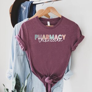 May include: A maroon t-shirt with the text "PHARMACY Technician" in colorful letters with a speckled pattern.