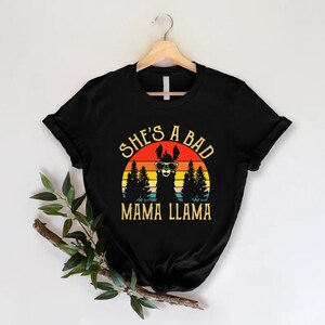 May include: Black t-shirt with a retro sunset graphic featuring a llama wearing sunglasses and the text "She's a Bad Mama Llama".