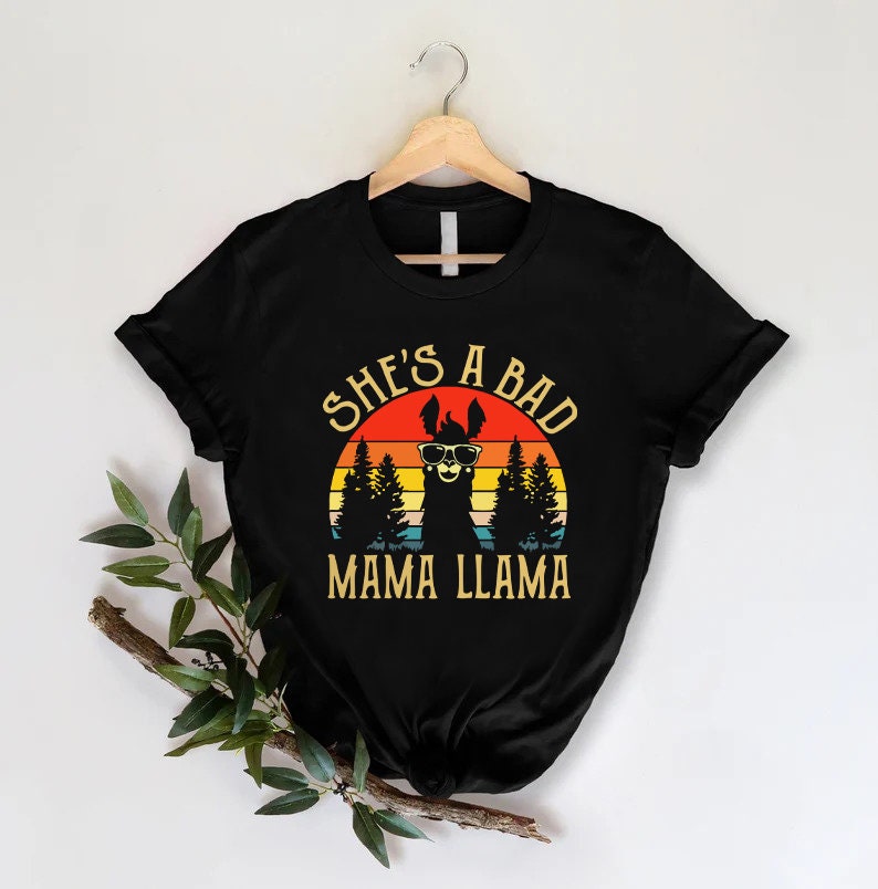 May include: Black t-shirt with a retro sunset graphic featuring a llama wearing sunglasses and the text "She's a Bad Mama Llama".