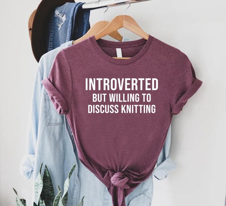 May include: A maroon t-shirt with the text "Introverted but willing to discuss knitting" in white.