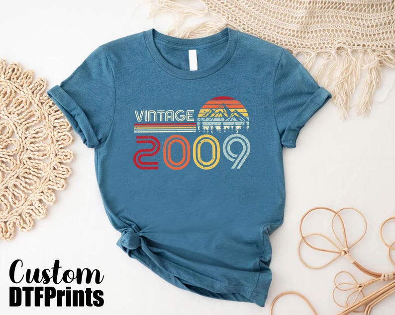 May include: A teal blue t-shirt with a vintage design featuring a mountain range and the text "Vintage 2009".