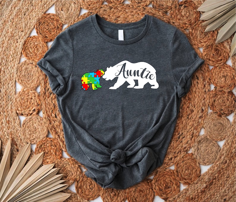 May include: A dark gray t-shirt with a white silhouette of a bear and a puzzle piece bear. The text "Auntie" is written on the bear.