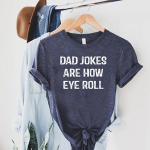 May include: A dark blue t-shirt with white text that reads "Dad Jokes Are How Eye Roll".