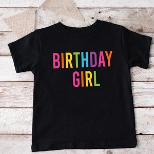 May include: Black t-shirt with the text "BIRTHDAY GIRL" in rainbow colors.
