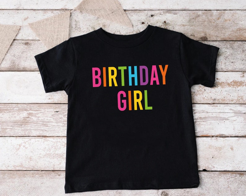 May include: Black t-shirt with the text "BIRTHDAY GIRL" in rainbow colors.