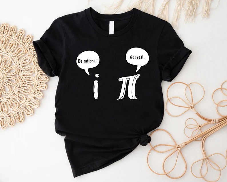 K&ouml;nnte beinhalten: Schwarzes T-Shirt mit einer wei&szlig;en Grafik der mathematischen Symbole 'i' und 'pi' mit Sprechblasen dar&uuml;ber. Die Sprechblase &uuml;ber 'i' sagt "Sei rational." und die Sprechblase &uuml;ber 'pi' sagt "Sei real."