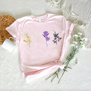 a pink t - shirt with flowers on it next to a basket of flowers