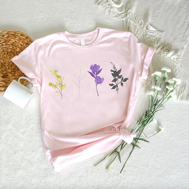 a pink t - shirt with flowers on it next to a basket of flowers