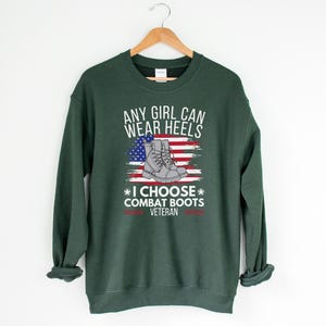 May include: Green sweatshirt with the text "Any girl can wear heels * I choose combat boots * Veteran" and a graphic of a pair of combat boots on an American flag.