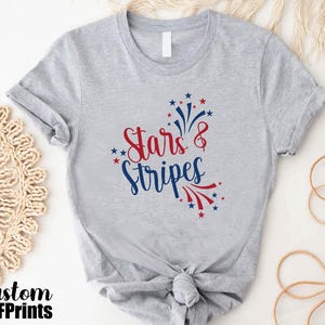 May include: Gray t-shirt with a red and blue graphic that says "Stars & Stripes" with a firework design.