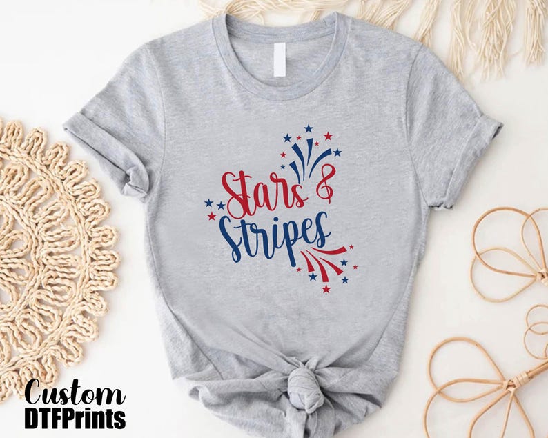 May include: Gray t-shirt with a red and blue graphic that says "Stars & Stripes" with a firework design.