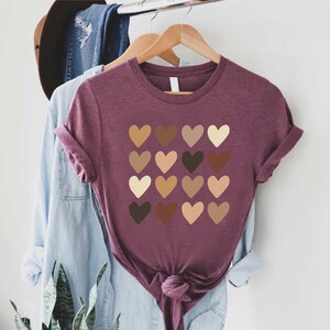 May include: A maroon t-shirt with a design of 16 hearts in different shades of brown, beige, and light brown.