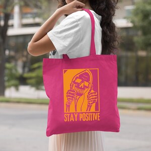 a woman holding a pink tote bag that says stay positive