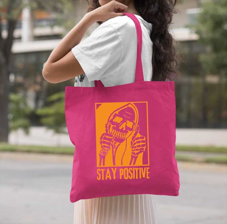 a woman holding a pink tote bag that says stay positive