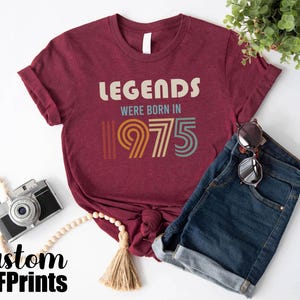 May include: A maroon t-shirt with the text "Legends were born in 1975" in a retro font with colorful accents.