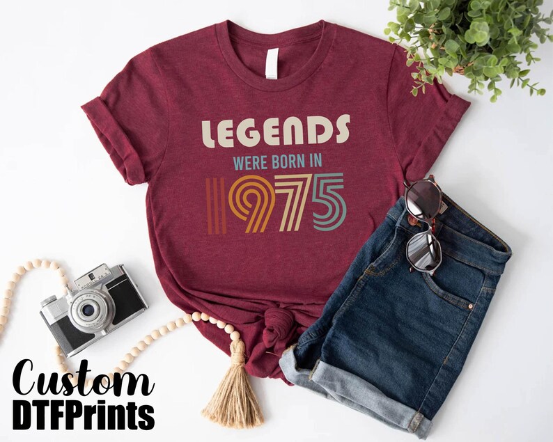 May include: A maroon t-shirt with the text "Legends were born in 1975" in a retro font with colorful accents.