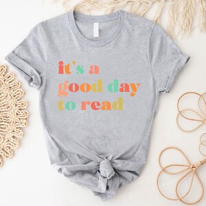 May include: Grey t-shirt with the text "it's a good day to read" in colourful letters.