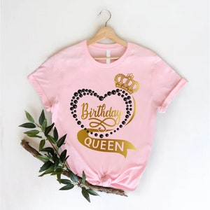 May include: Pink t-shirt with a gold heart design and the text "Birthday Queen". The heart is made of black beads and has a gold crown on top.
