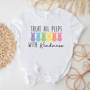 May include: White t-shirt with a graphic of colourful Peeps candy and the text "Treat all peeps with kindness."