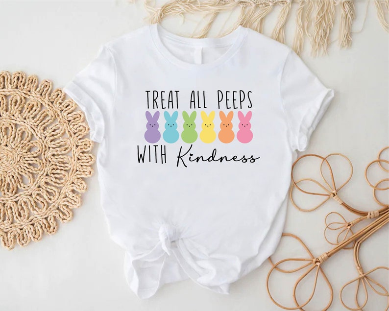 May include: White t-shirt with a graphic of colourful Peeps candy and the text "Treat all peeps with kindness."