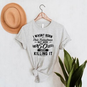Pode incluir: Camiseta cinza com texto preto que diz "Eu n&atilde;o nasci assim, mas aqui estou, 50 anos depois e estou arrasando".