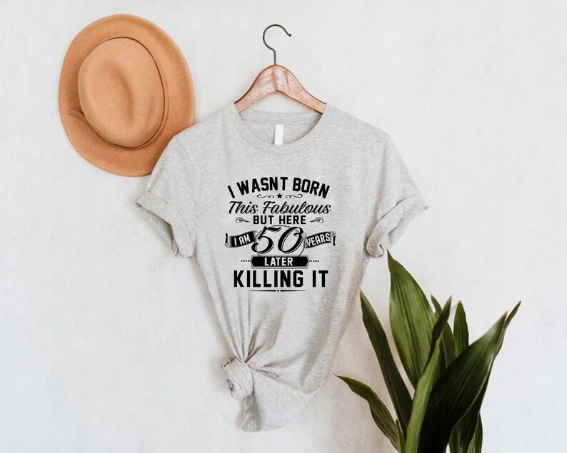 Pode incluir: Camiseta cinza com texto preto que diz "Eu n&atilde;o nasci assim, mas aqui estou, 50 anos depois e estou arrasando".