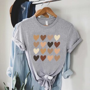 May include: A gray t-shirt with a design of 16 brown, beige, and cream hearts arranged in a grid.