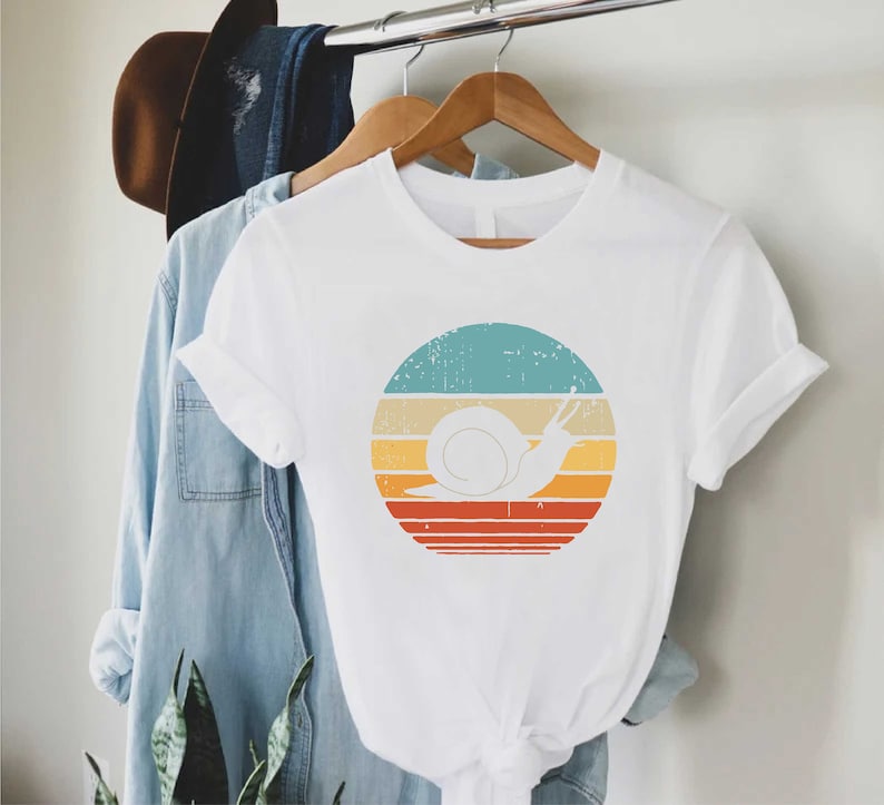 a t - shirt hanging on a clothes rack next to a plant