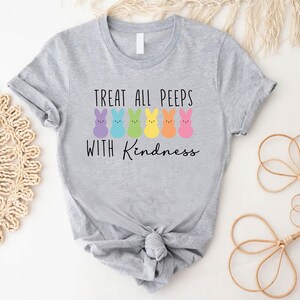 May include: A grey t-shirt with a graphic of colourful Peeps and the text "Treat all peeps with kindness".