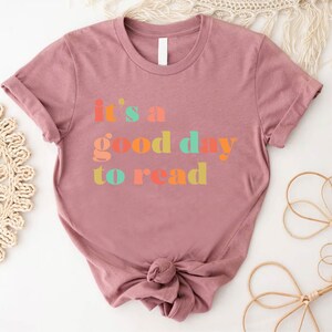 May include: A mauve t-shirt with the text "it's a good day to read" in colourful letters.