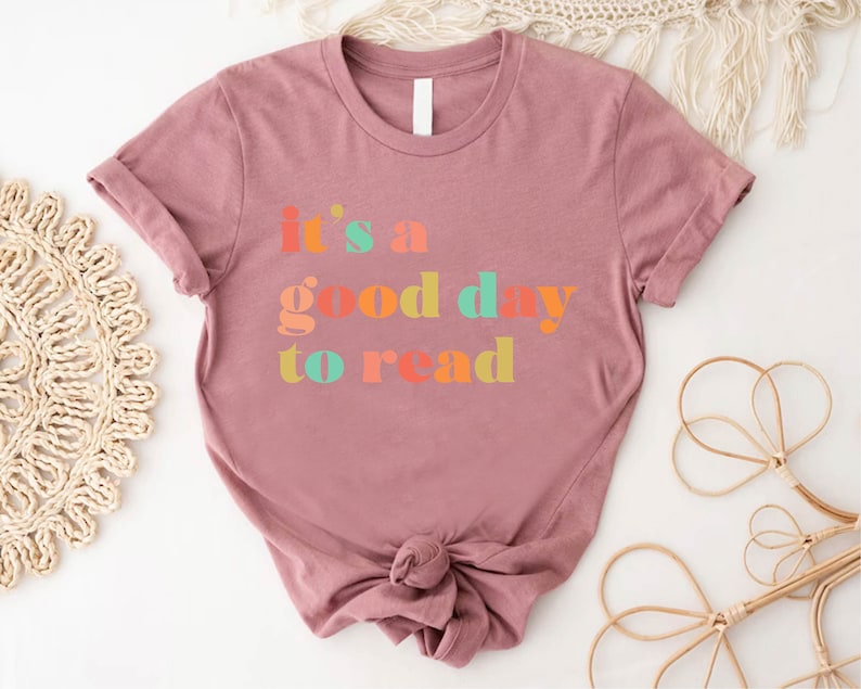 May include: A mauve t-shirt with the text "it's a good day to read" in colourful letters.